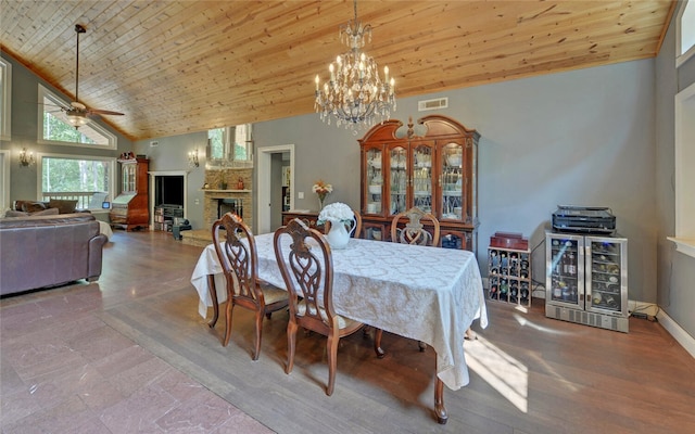 dining area featuring wood ceiling, high vaulted ceiling, a large fireplace, ceiling fan with notable chandelier, and light hardwood / wood-style floors