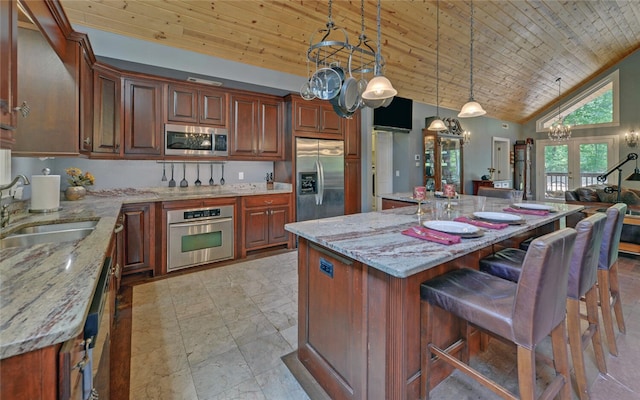 kitchen with sink, decorative light fixtures, stainless steel appliances, a center island, and light stone countertops