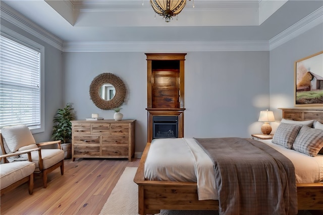 bedroom with light wood-type flooring, crown molding, and a tray ceiling