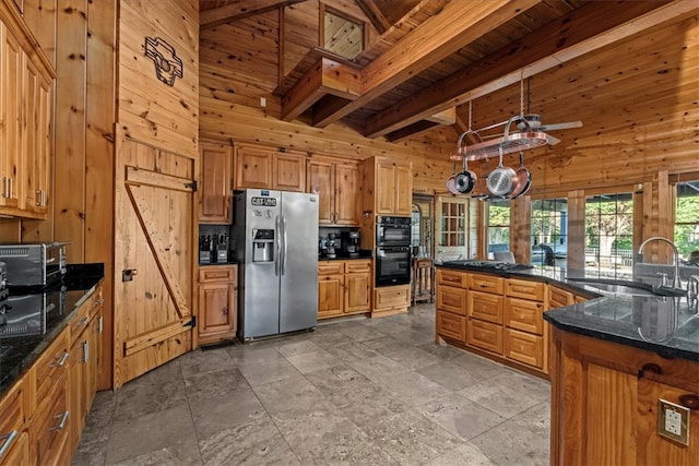 kitchen with wood walls, beam ceiling, sink, black appliances, and a high ceiling