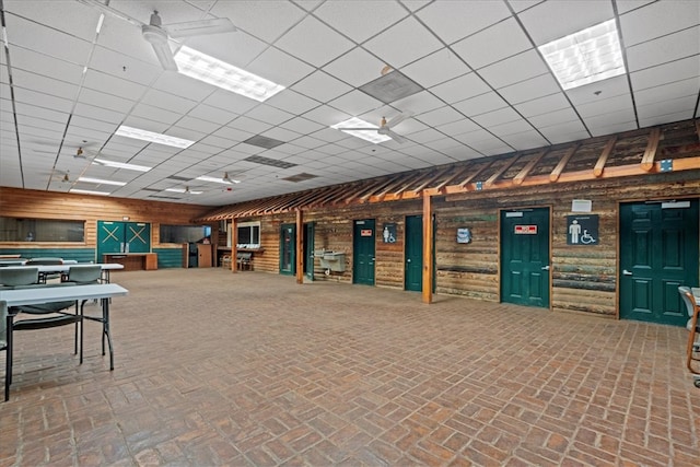 interior space with wood walls, ceiling fan, and a paneled ceiling