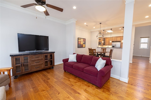 living room featuring ceiling fan, light wood-type flooring, crown molding, and decorative columns