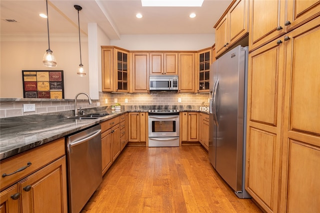 kitchen with sink, light hardwood / wood-style flooring, appliances with stainless steel finishes, decorative light fixtures, and dark stone countertops