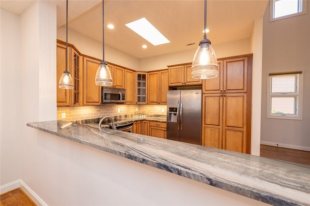 kitchen with pendant lighting, dark stone counters, kitchen peninsula, stainless steel appliances, and backsplash