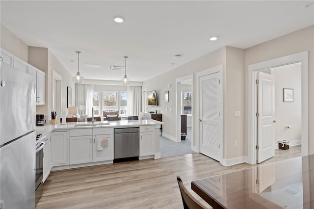 kitchen featuring kitchen peninsula, appliances with stainless steel finishes, light hardwood / wood-style floors, white cabinetry, and hanging light fixtures