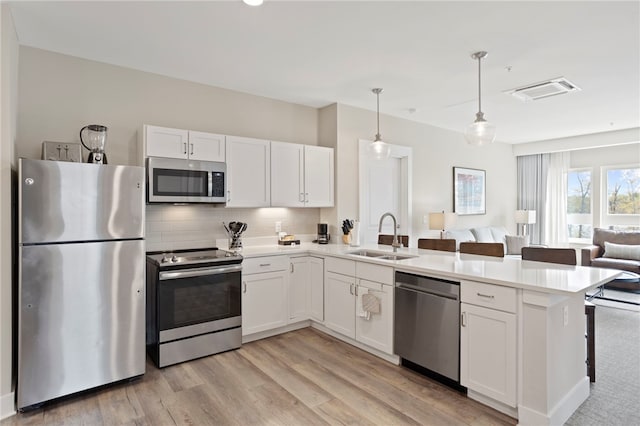 kitchen with appliances with stainless steel finishes, sink, light hardwood / wood-style floors, white cabinetry, and hanging light fixtures