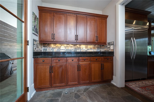 kitchen with dark stone countertops, stainless steel built in refrigerator, and backsplash