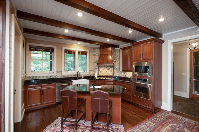 kitchen with appliances with stainless steel finishes, backsplash, custom exhaust hood, a center island with sink, and dark hardwood / wood-style floors