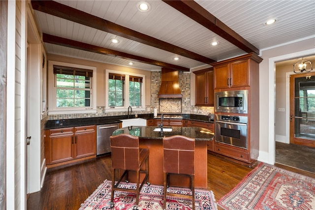 kitchen with dark wood-type flooring, custom range hood, a kitchen breakfast bar, a center island with sink, and appliances with stainless steel finishes