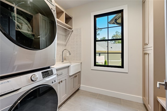 washroom with cabinets, light tile patterned floors, stacked washer / drying machine, and sink