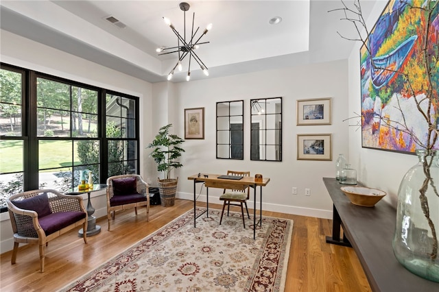 office space featuring light wood-type flooring, a raised ceiling, and a notable chandelier