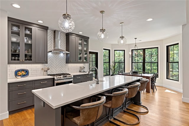 kitchen with sink, wall chimney range hood, high end stove, a large island with sink, and light hardwood / wood-style floors