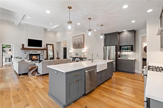 kitchen featuring sink, stainless steel appliances, an island with sink, decorative light fixtures, and light wood-type flooring