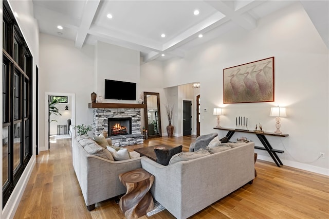 living room with beam ceiling, a fireplace, light hardwood / wood-style flooring, and a towering ceiling