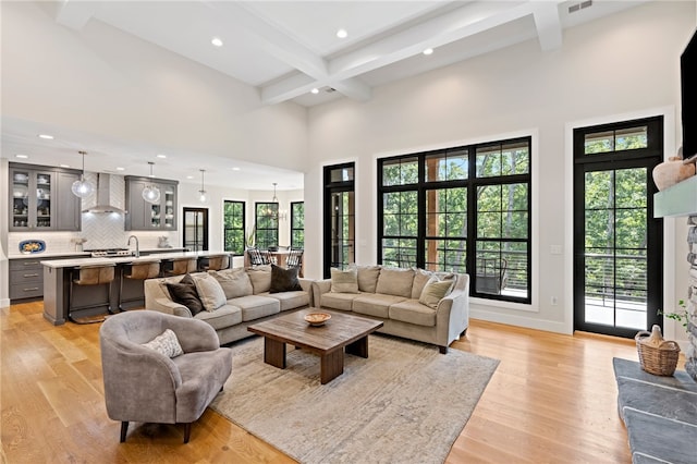 living room featuring beam ceiling, a towering ceiling, light hardwood / wood-style flooring, and coffered ceiling