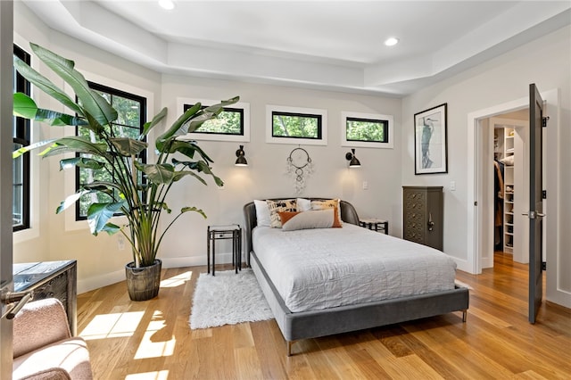 bedroom featuring multiple windows, light wood-type flooring, and a tray ceiling