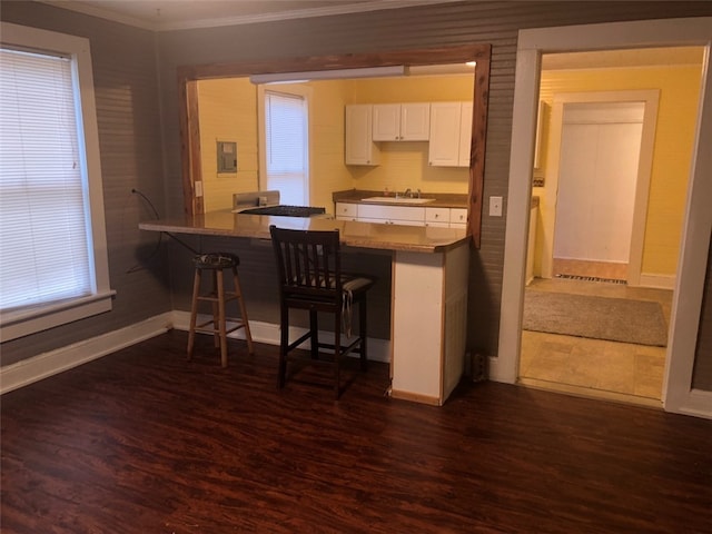 kitchen with sink, kitchen peninsula, dark wood-type flooring, white cabinetry, and a breakfast bar area