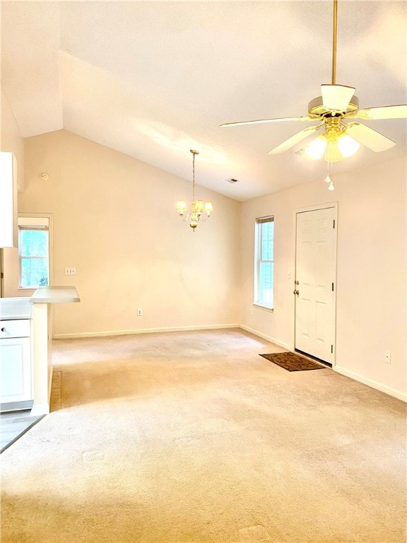 carpeted spare room with ceiling fan with notable chandelier, vaulted ceiling, and a healthy amount of sunlight