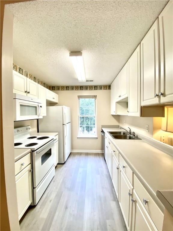 kitchen featuring sink, a textured ceiling, white appliances, white cabinets, and light wood-type flooring