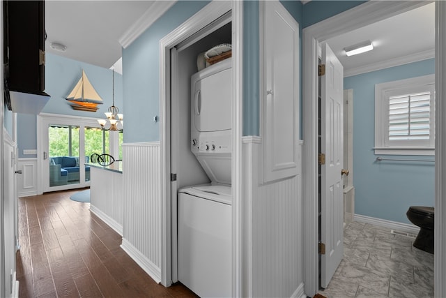 clothes washing area featuring crown molding, an inviting chandelier, wood-type flooring, and stacked washer / drying machine