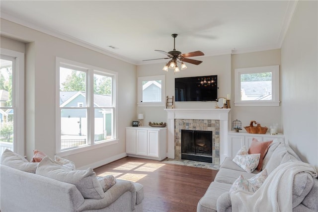 living room with a tile fireplace, light wood-type flooring, ceiling fan, and crown molding