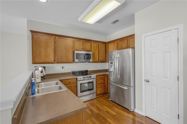 kitchen with appliances with stainless steel finishes, sink, and light hardwood / wood-style flooring