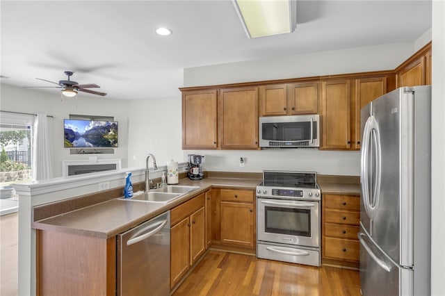 kitchen with light wood-type flooring, sink, kitchen peninsula, appliances with stainless steel finishes, and ceiling fan