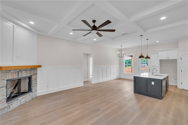 kitchen with light wood-type flooring, white cabinets, an island with sink, and decorative light fixtures