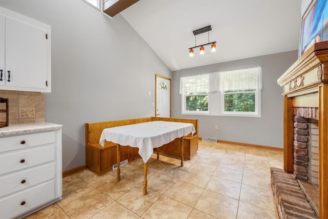 tiled dining space with lofted ceiling and a brick fireplace