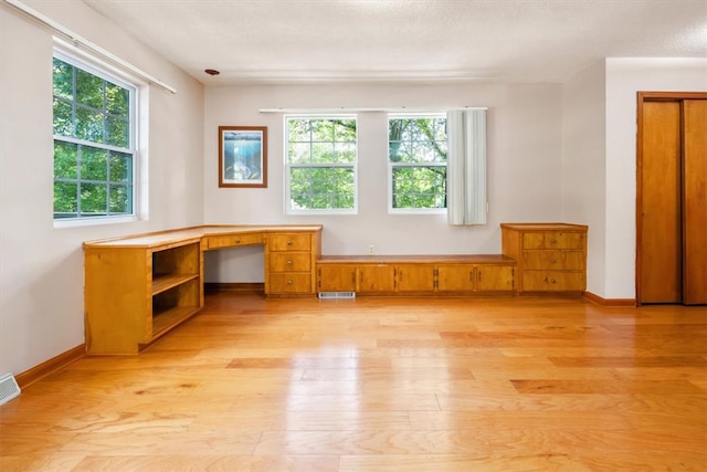 unfurnished office featuring light hardwood / wood-style flooring, built in desk, and plenty of natural light