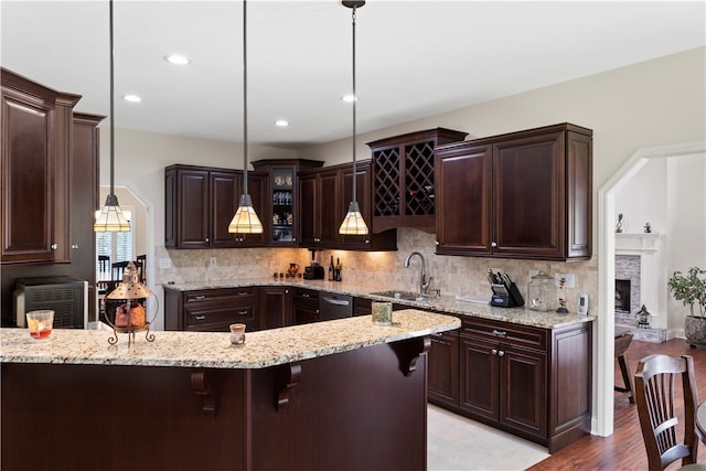 kitchen with sink, hanging light fixtures, a breakfast bar area, a fireplace, and dark brown cabinets