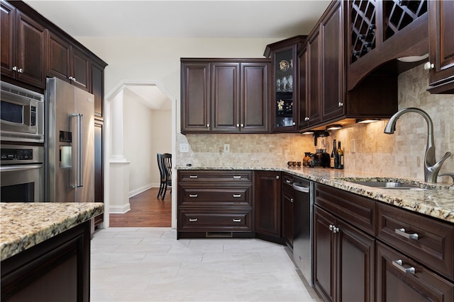 kitchen with sink, light stone counters, decorative backsplash, dark brown cabinets, and appliances with stainless steel finishes