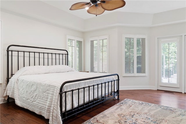 bedroom with ceiling fan, multiple windows, dark wood-type flooring, and a tray ceiling