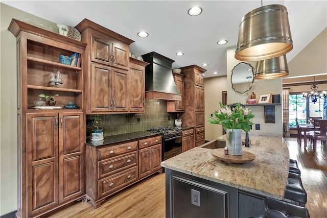 kitchen featuring a breakfast bar, dark stone counters, custom exhaust hood, light hardwood / wood-style flooring, and black gas range