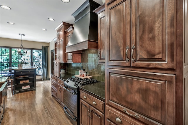 kitchen featuring light hardwood / wood-style floors, tasteful backsplash, an inviting chandelier, black gas range, and premium range hood