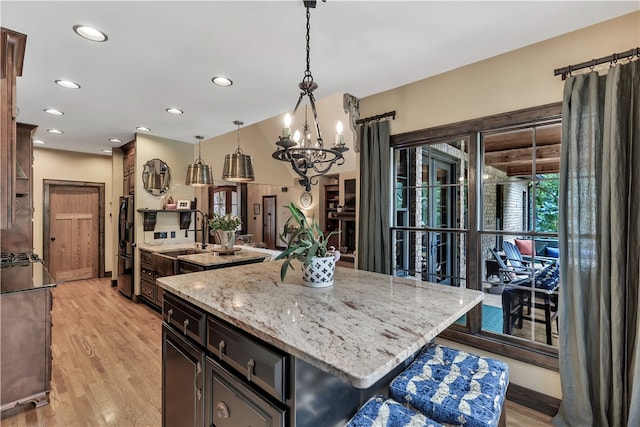 kitchen featuring hanging light fixtures, a large island with sink, light stone counters, light wood-type flooring, and an inviting chandelier