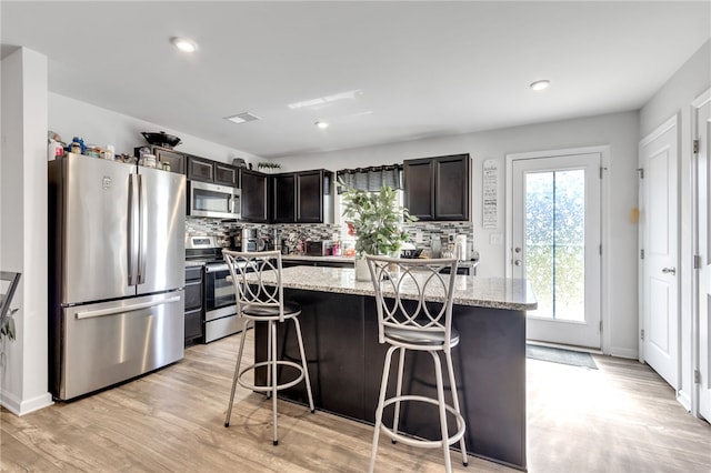 kitchen with a breakfast bar, light stone counters, light hardwood / wood-style floors, a center island, and stainless steel appliances