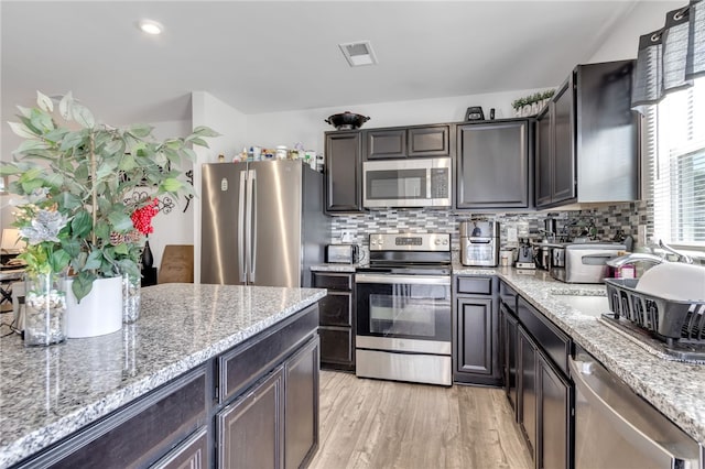 kitchen with backsplash, light stone countertops, light hardwood / wood-style flooring, and stainless steel appliances