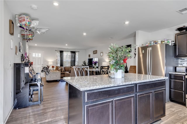 kitchen with light wood-type flooring, light stone counters, a center island, and dark brown cabinetry