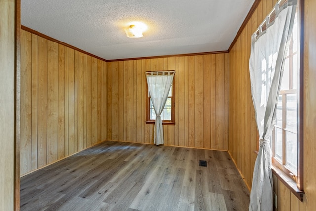 empty room featuring ornamental molding, wood walls, and hardwood / wood-style floors