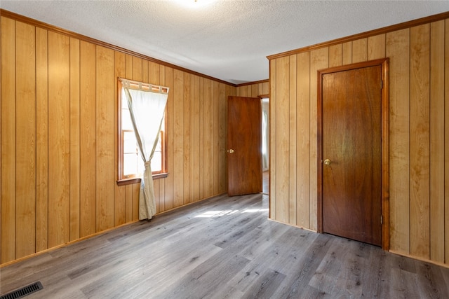 unfurnished bedroom featuring a textured ceiling, light hardwood / wood-style floors, and wood walls