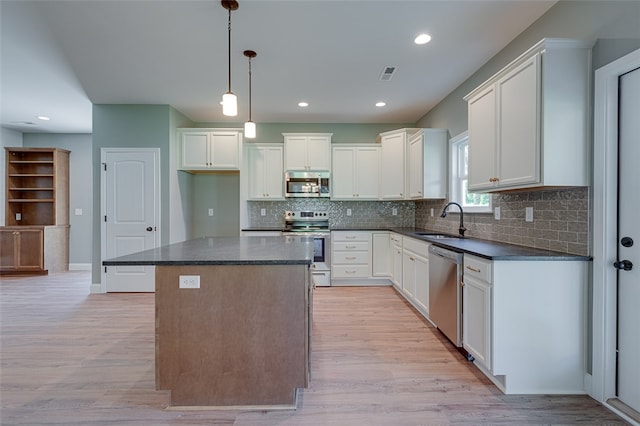 kitchen with appliances with stainless steel finishes, white cabinetry, a kitchen island, light wood-type flooring, and sink