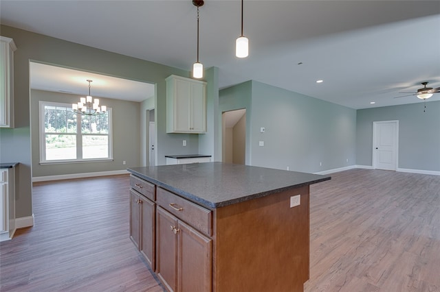 kitchen featuring ceiling fan with notable chandelier, light hardwood / wood-style floors, a center island, and decorative light fixtures