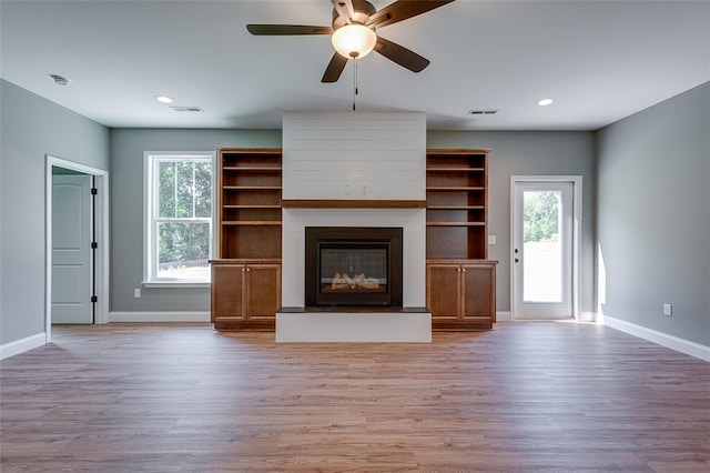 unfurnished living room with light hardwood / wood-style floors, a large fireplace, and ceiling fan