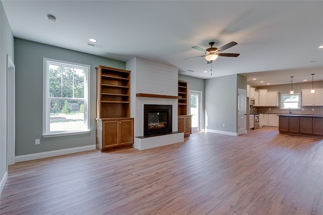 unfurnished living room with ceiling fan, light hardwood / wood-style flooring, a fireplace, and a healthy amount of sunlight