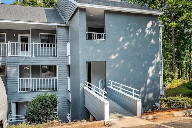 exterior space with a shingled roof, stairway, and stucco siding