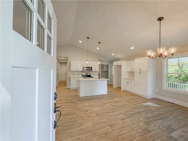 kitchen featuring light wood-type flooring, a center island with sink, decorative light fixtures, white cabinets, and appliances with stainless steel finishes