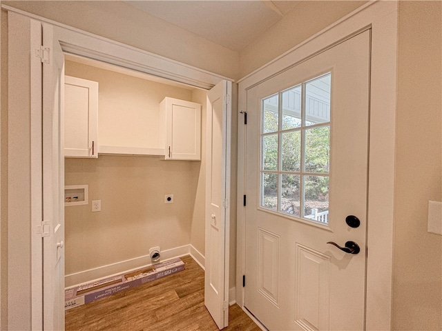 washroom featuring electric dryer hookup, a healthy amount of sunlight, hardwood / wood-style floors, and cabinets