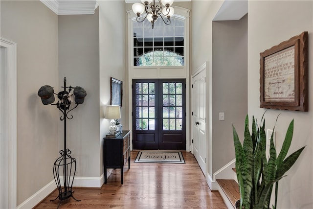 foyer entrance featuring a towering ceiling, crown molding, french doors, hardwood / wood-style flooring, and a chandelier