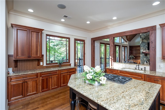 kitchen with dark hardwood / wood-style floors, light stone counters, a breakfast bar, stainless steel gas stovetop, and sink